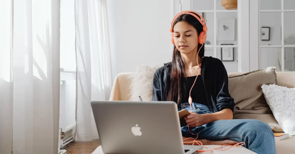 Jovem mulher sentada no sofá com fones de ouvido em frente ao seu laptop aprendendo como criar vídeo com roteiro com IA gratuito
