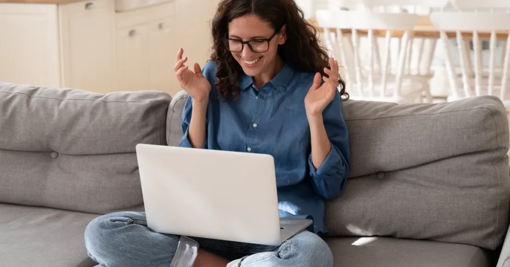 Mulher vestindo camisa azul e jeans, sentada no sofá da sala com seu laptop no colo surpresa porque aprendeu como animar uma imagem com IA
