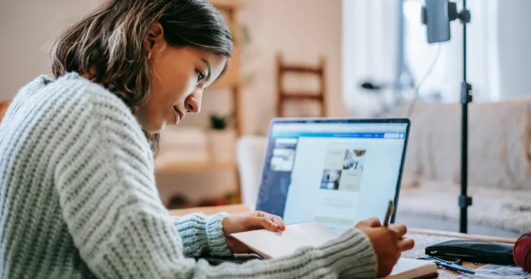 Mulher sentada à mesa de casa, com laptop na mesa, anotando ideias da Inteligência Artificial Para Negócios Online