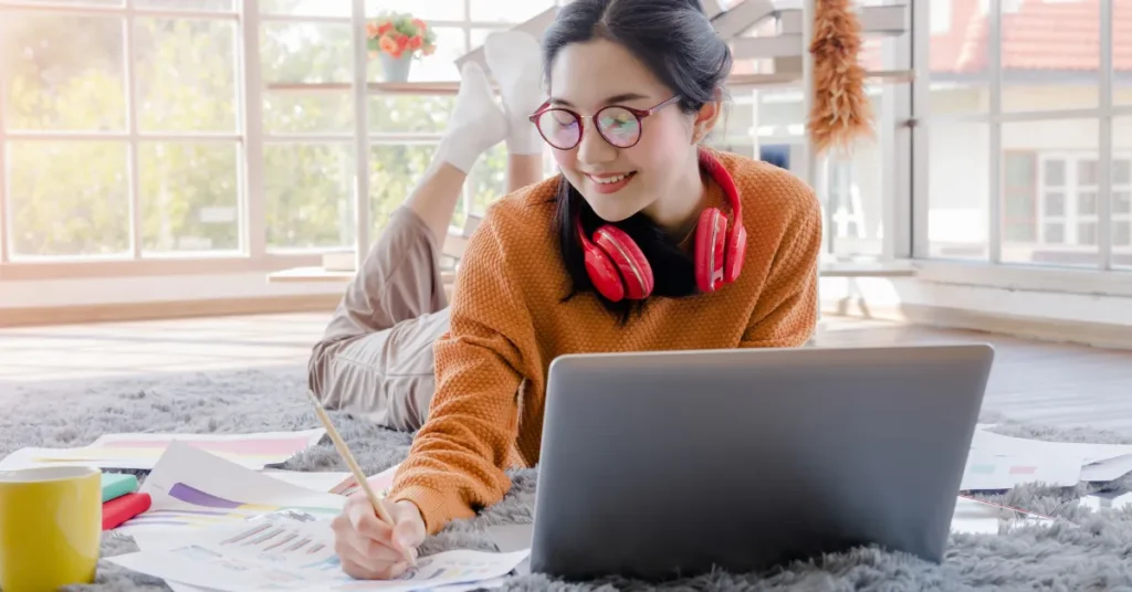 Jovem mulher deitada no tapete com laptop, lápis, papel e café representando como a IA pode transformar o futuro da educação