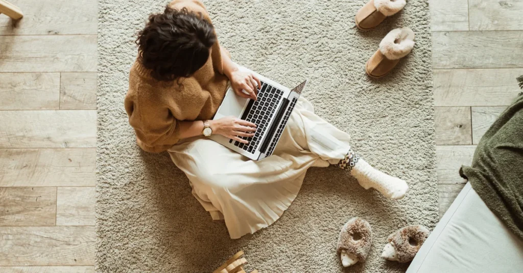 Mulher sentada no tapete da sala com laptop no colo vestindo roupas confortáveis representando como a IA faz parte da rotina e a ideia de inteligência artificial descomplicada