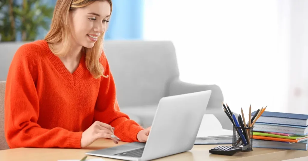 Pedagoga trabalhando em sua mesa com livros, cadernos, lápis, calculadora e seu laptop representando como a IA pode ajudar o professor