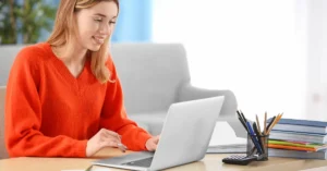 Pedagoga trabalhando em sua mesa com livros, cadernos, lápis, calculadora e seu laptop representando como a IA pode ajudar o professor